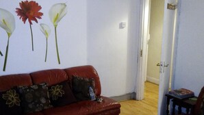 En stue med en rød lædersofa, et lille bord og en væg med blomstermotiver.