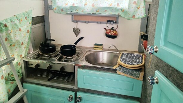 Una kitchenette compacta con estufa a gas, dos ollas, un lavamanos y una pequeña encimera.