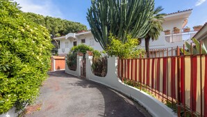 A narrow street with a white building, a red and beige fence, and green foliage. - Quiet Apartment by Wonderful Italy (Sanremo)