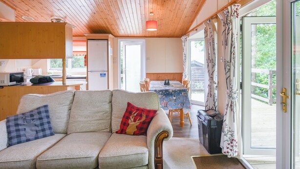 Interior acogedor de una cabaña con sofá, mesa de comedor, zona de cocina y puerta corrediza de vidrio que da a una terraza exterior.
