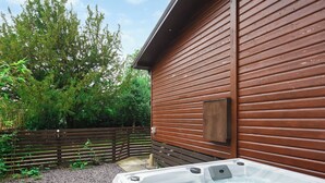 Un jacuzzi al aire libre frente a una cabaña de madera, con una valla de madera y árboles al fondo.