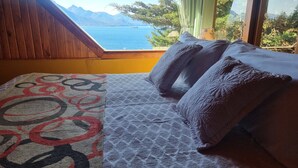 Ein Schlafzimmer mit Seeblick und Blick auf Berge, ein Bett mit gemusterten Textilien und einer Holzzielende.