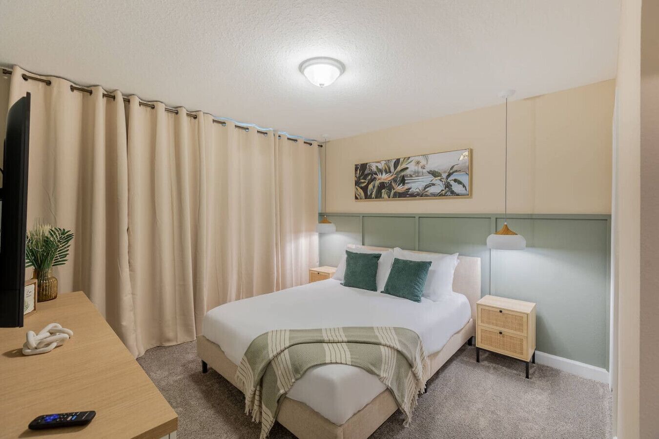 Une chambre d’hôtel avec un lit, des tables de chevet, un bureau, une lampe, un tableau et un rideau.