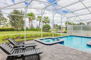 A covered outdoor swimming pool with lounge chairs, surrounded by greenery and palm trees. - Cozy House w/ Game Room, Theater, Pool & More! (Davenport)