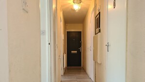 Un couloir étroit avec un plancher en bois, des murs blancs et un lustre.