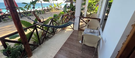 Un balcón con vista a la playa, una hamaca y una mesa con sillas.