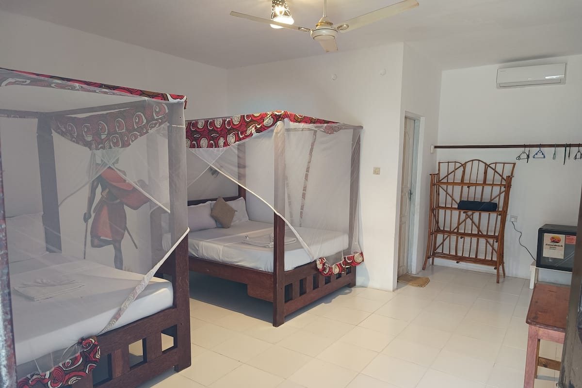 Habitació amb dos llits de fusta, mosquiteres, ventilador de sostre i una cadira de fusta.