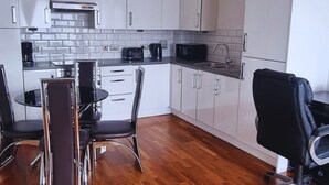 Una cucina moderna con mobili bianchi, un piano di lavoro nero e un'area pranzo con tavolo in vetro e sedie nere.