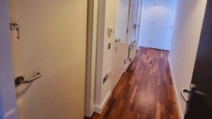 Un corridoio con pavimento in legno, pareti bianche e un lampadario al soffitto.