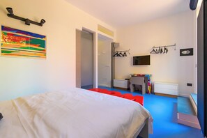 Un dormitorio con una cama, televisión, escritorio y un cuadro de colores.
