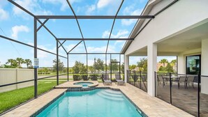 Une piscine avec un jacuzzi, entourée d’un patio couvert aménagé avec du mobilier d’extérieur.
