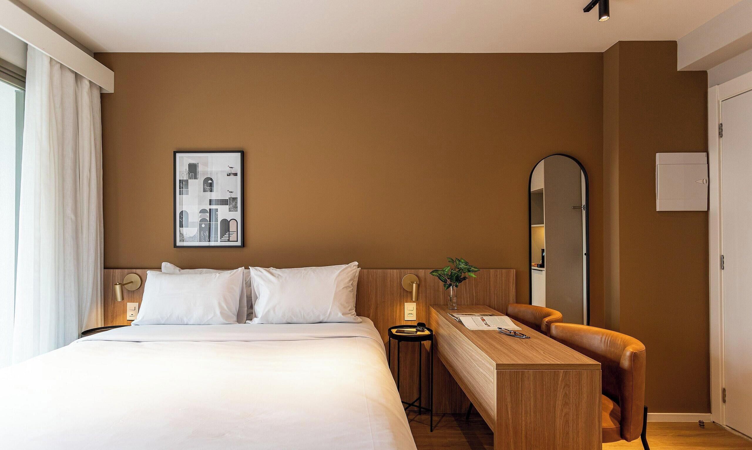 A hotel room with a bed, a desk, a mirror, and a framed picture on the wall.