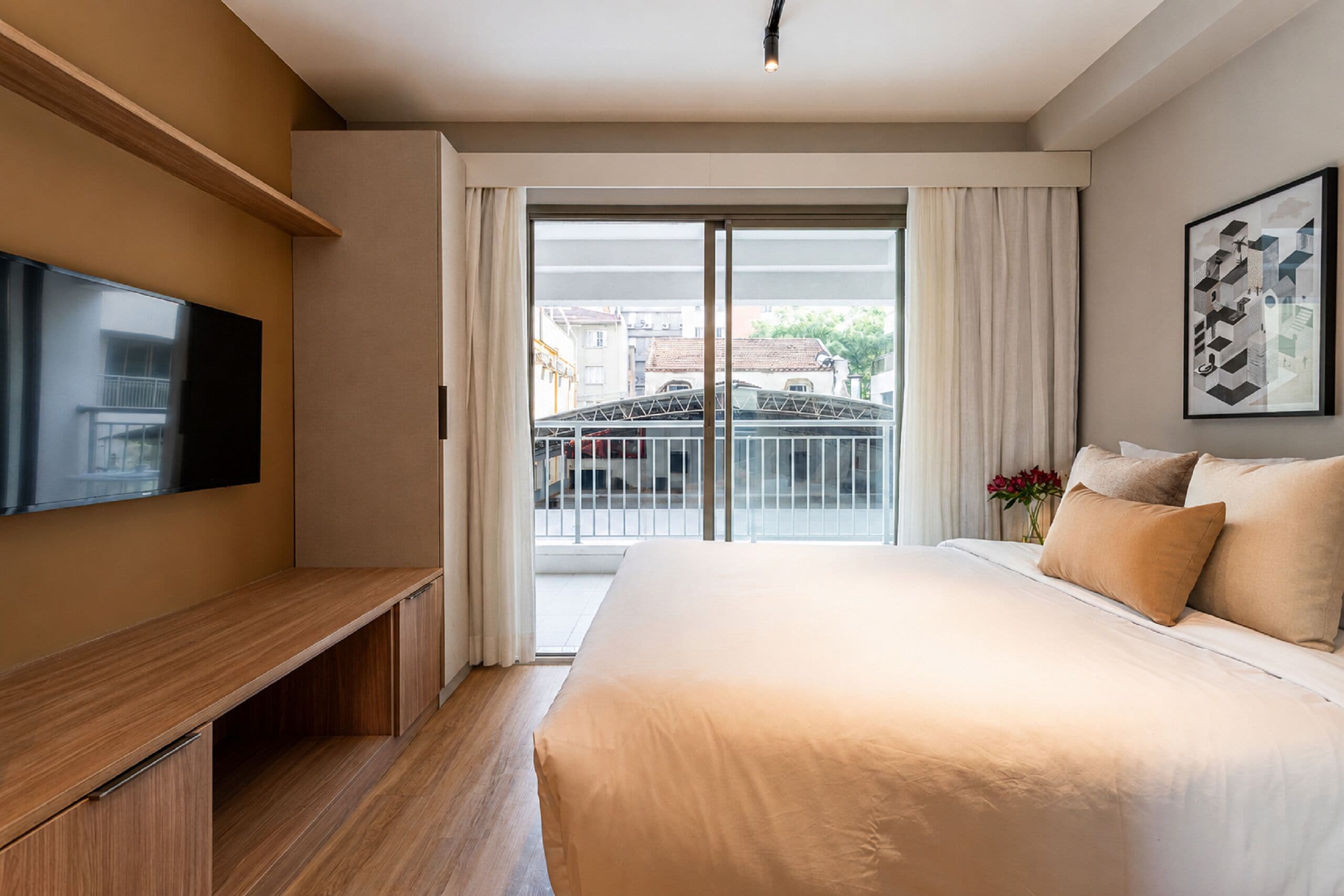 Camera d'albergo con un letto grande, una TV a parete, un balcone con vista sugli edifici e un quadro appeso alla parete.
