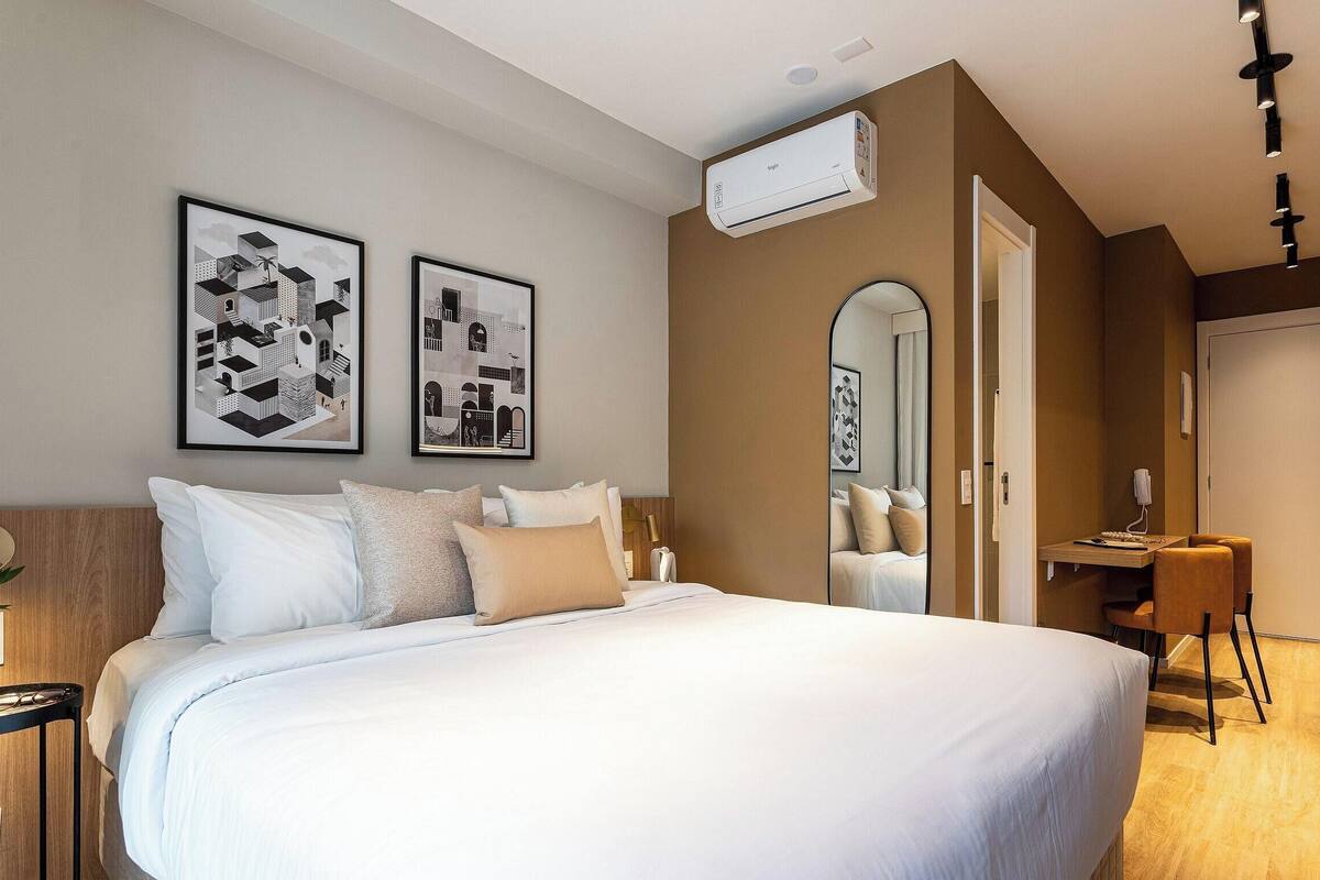 Une chambre d’hôtel moderne avec un grand lit, un bureau et deux œuvres d’art encadrées accrochées au mur.