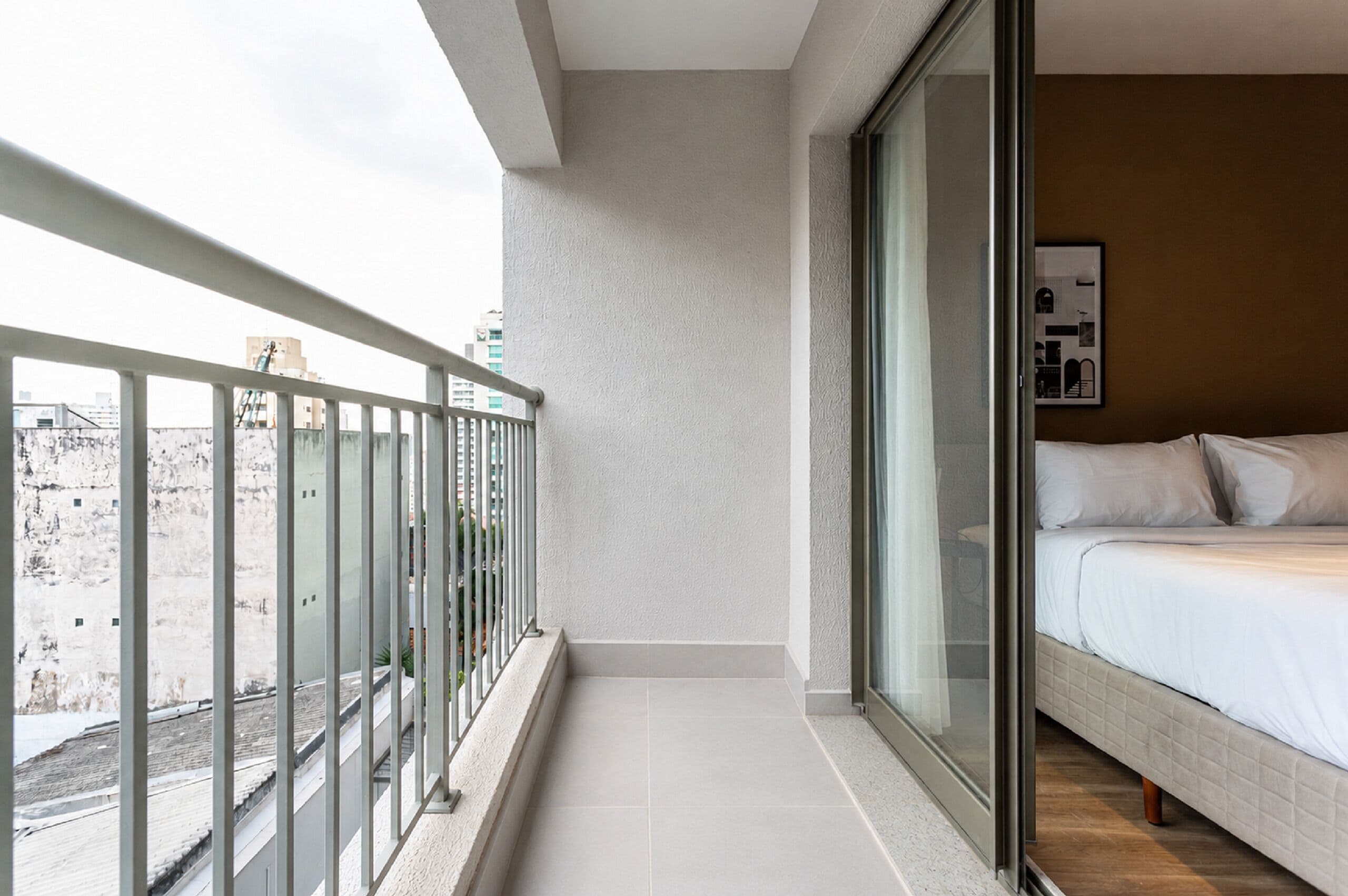 Un balcon avec une balustrade en métal, un lit avec une literie blanche et une vue sur les immeubles.