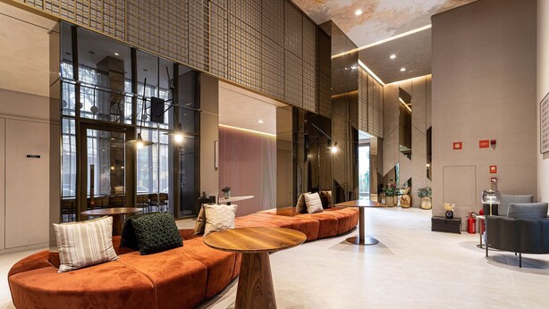 Eine moderne Lobby mit einer gebogenen, orangefarbenen Couch, einem runden Holztisch und einer großen Glaswand.