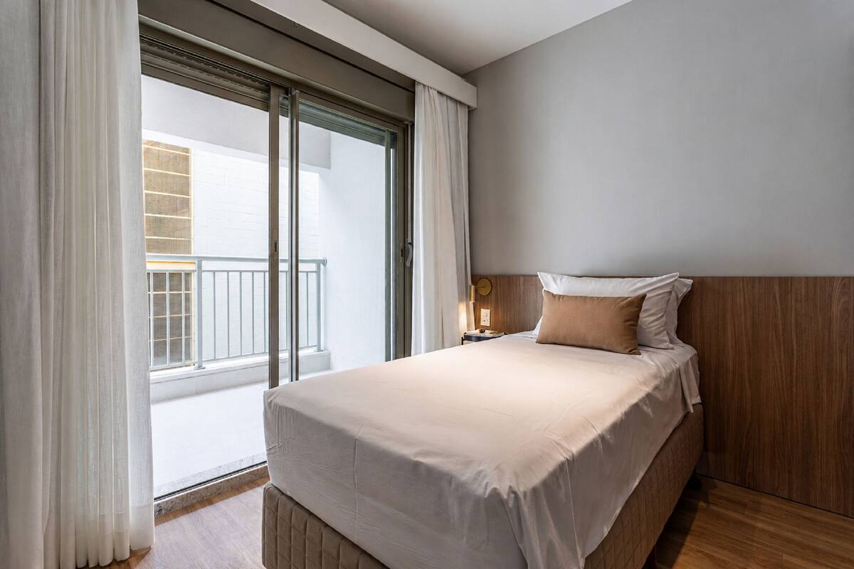 Une chambre d’hôtel avec un lit, une table de chevet, une fenêtre avec des rideaux et une vue sur un balcon.