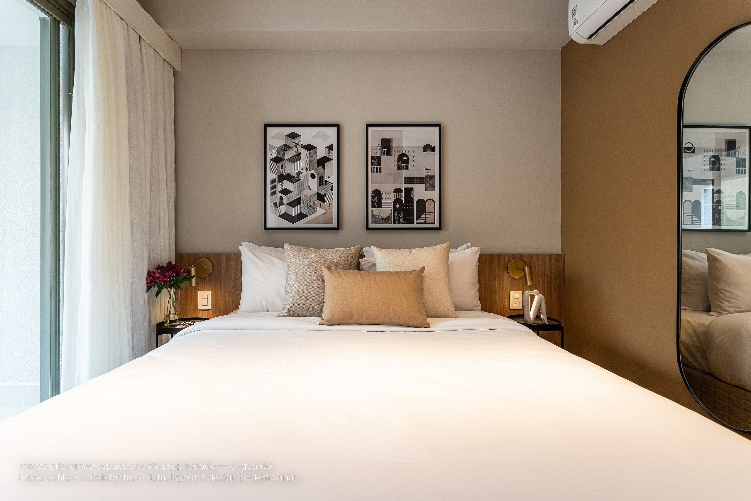 Habitación de hotel con una cama grande, dos cuadros enmarcados en la pared, una mesita de noche con una lámpara y un espejo.