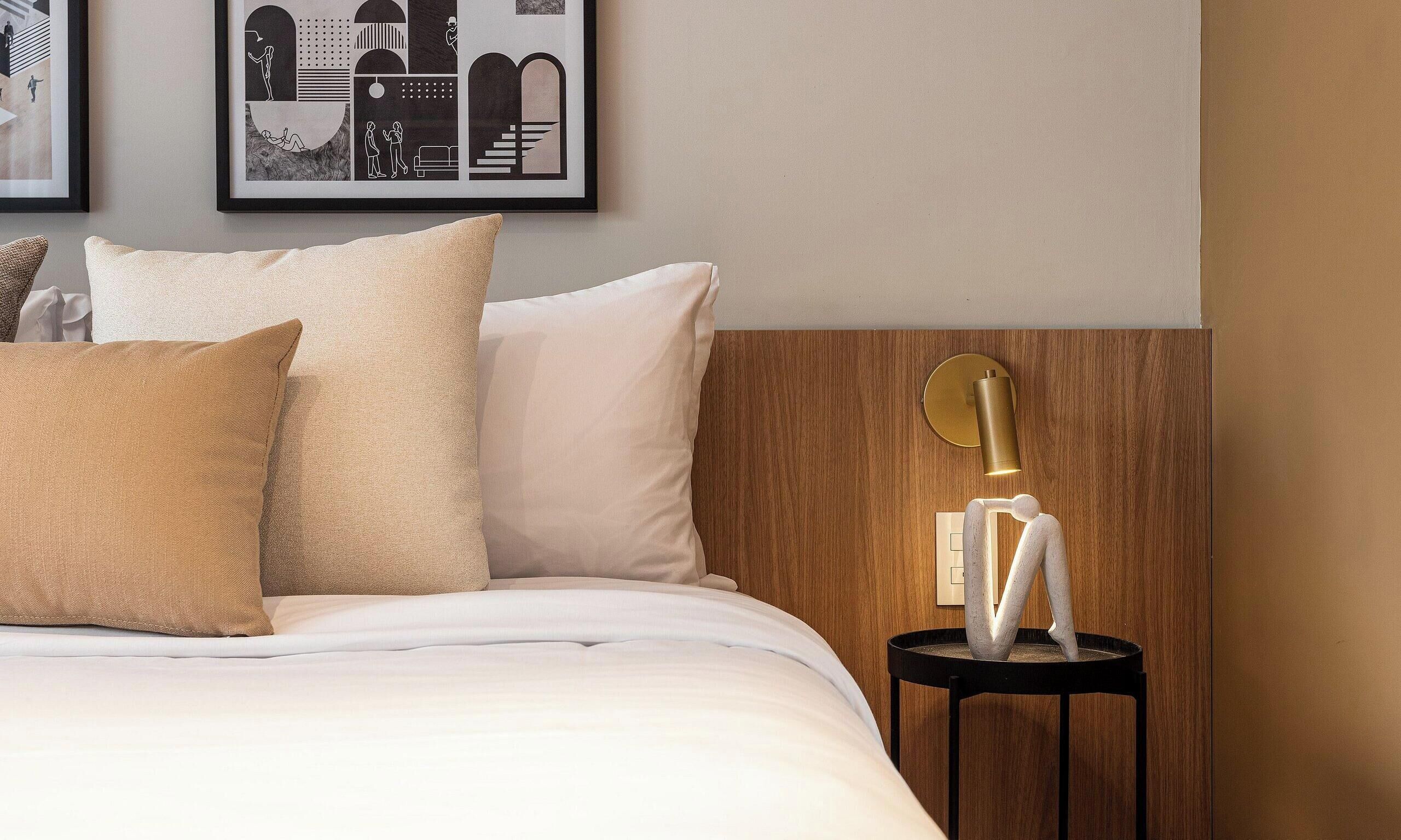 Un lit bien fait, avec des oreillers, une tête de lit en bois et un luminaire fixé au mur.