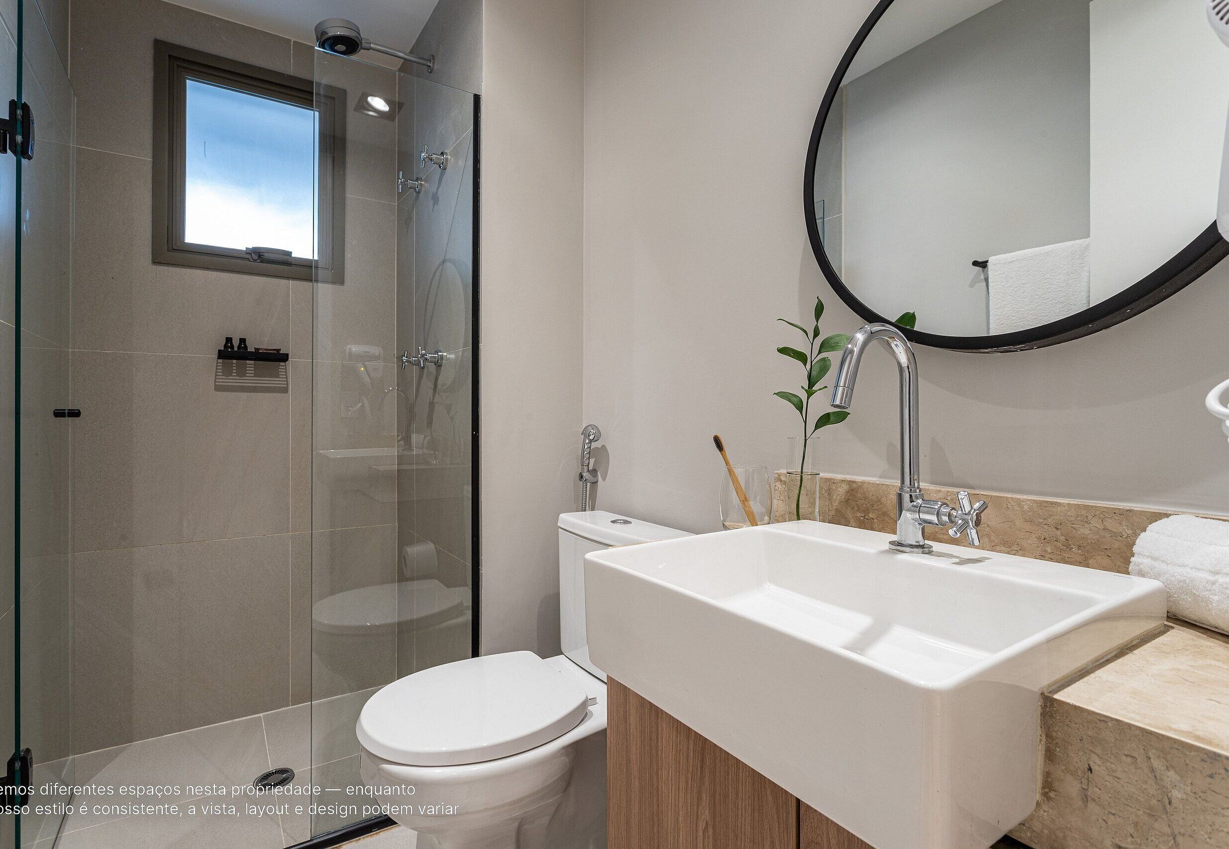 Een moderne badkamer met een douchecabine van glas, een wit toilet, een wastafel met spiegel en een klein raam boven de douche.