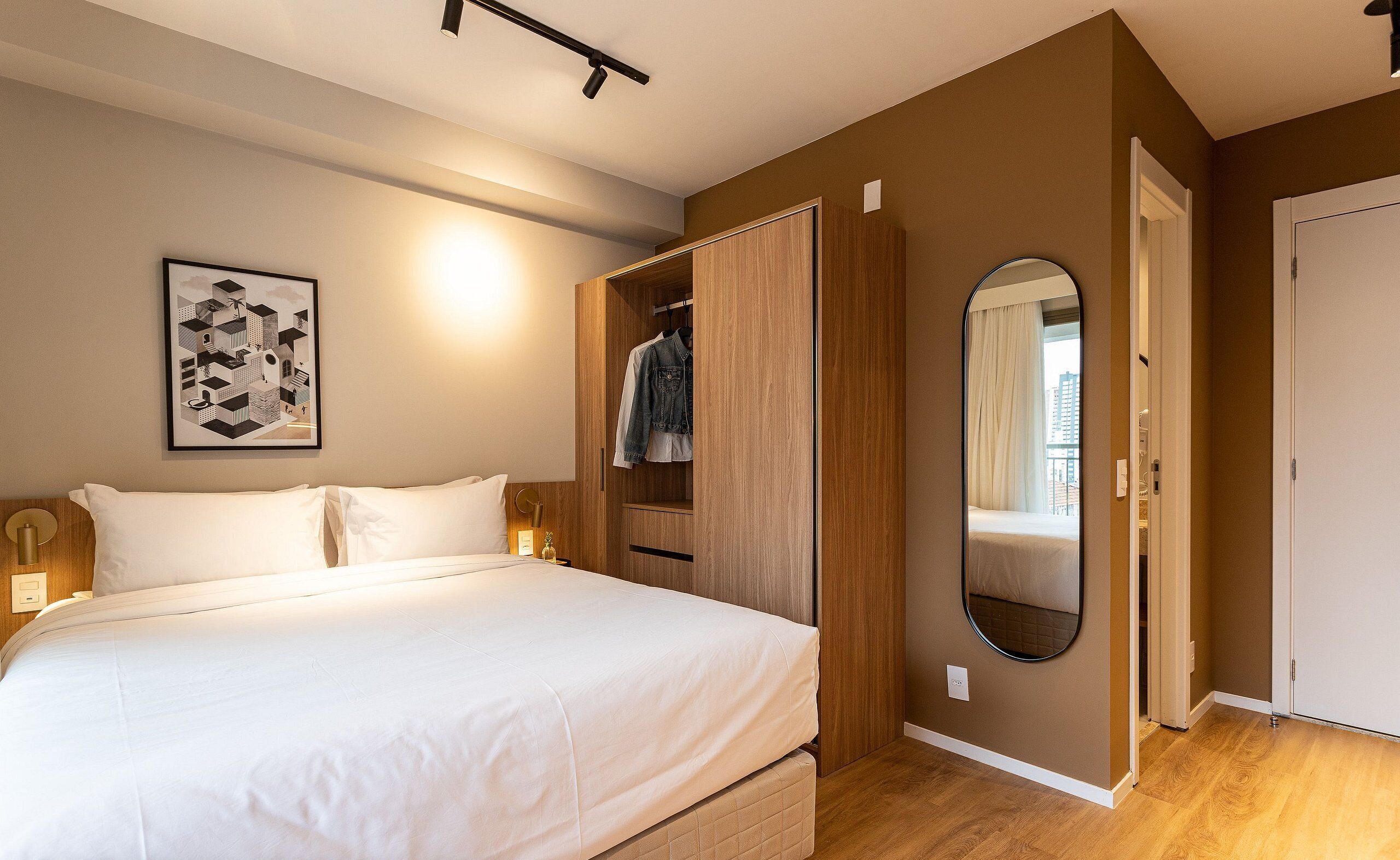 A bedroom with a bed, a wardrobe, a mirror, and a wall-mounted light fixture.