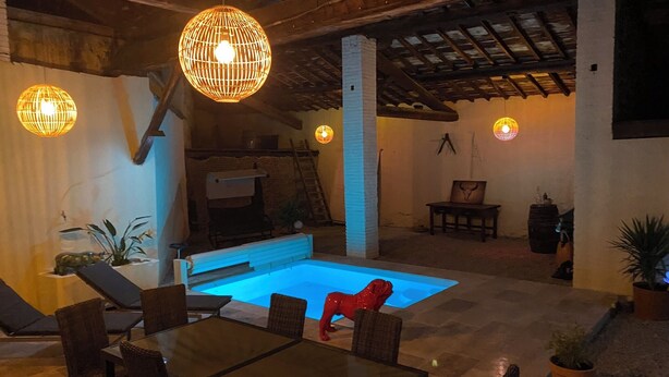 Zona de piscina con mobiliario de mimbre e iluminación colgante.