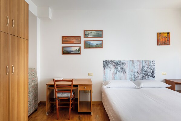Un dormitorio con una cama, un escritorio y una silla. Hay cuatro cuadros enmarcados en la pared.
