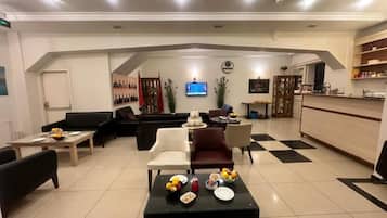 A spacious living area with a kitchen in the background, a flat-screen TV mounted on the wall, and a variety of seating options including sofas and chairs.