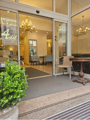 A hotel entrance with glass doors, a reception area, and a dining area with chairs and a table. - Adil Konak Hotel (Istanbul)