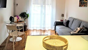 A modern living room with a grey sofa, a round woven coffee table, and a dining area with a glass table and chairs. - Athens White House 🏠  (Athina)