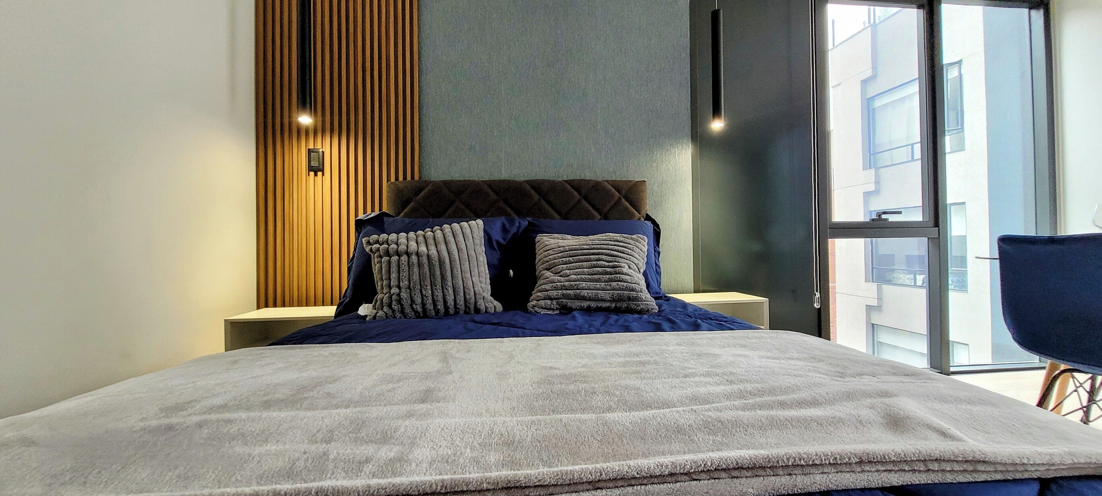 Une chambre moderne avec un grand lit, un mur recouvert de panneaux en bois et une vue sur la ville, visible à travers une grande fenêtre.