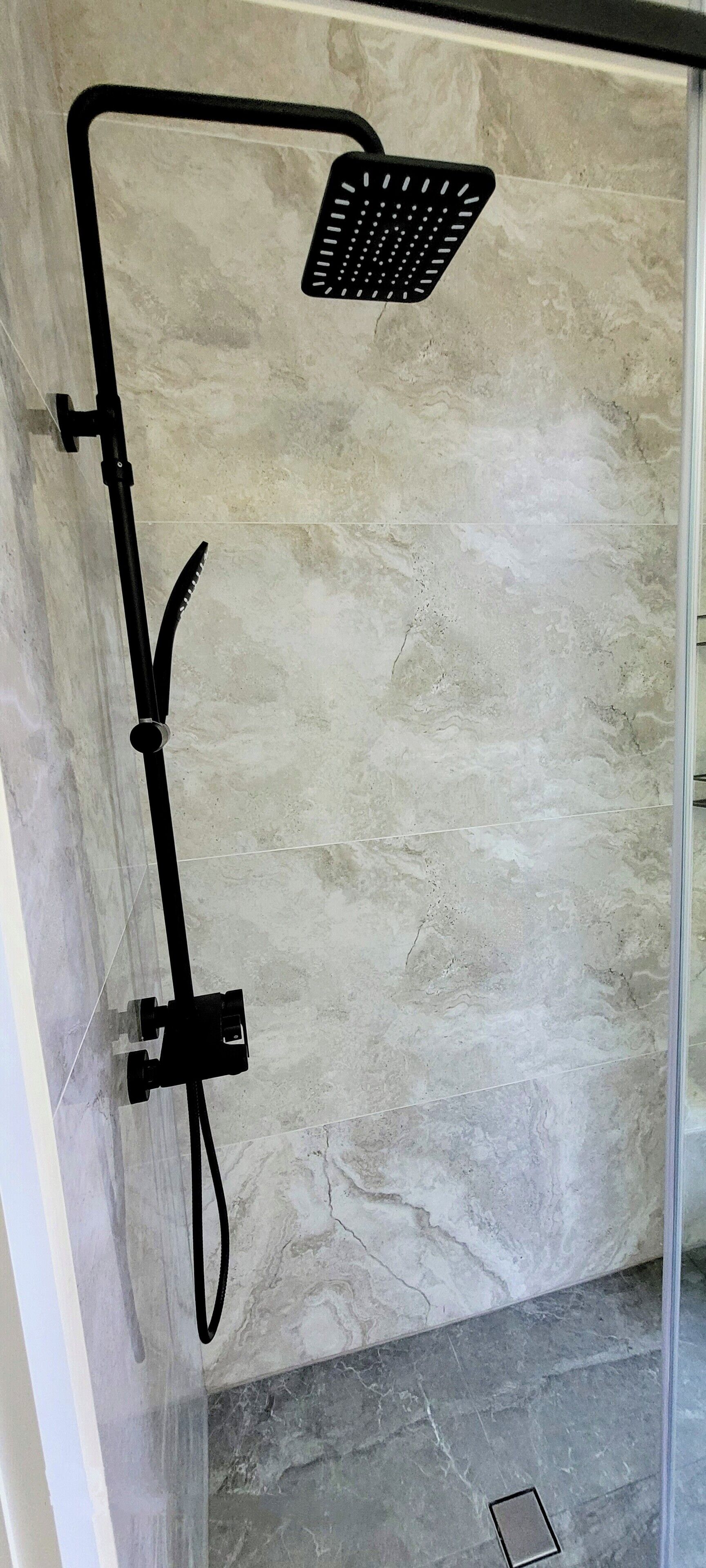 A shower with a black hose and a square showerhead mounted on a wall with a marble-like texture.