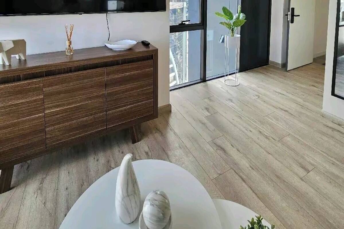 A modern living room with a large TV, wooden furniture, and a view of a cityscape through large windows.