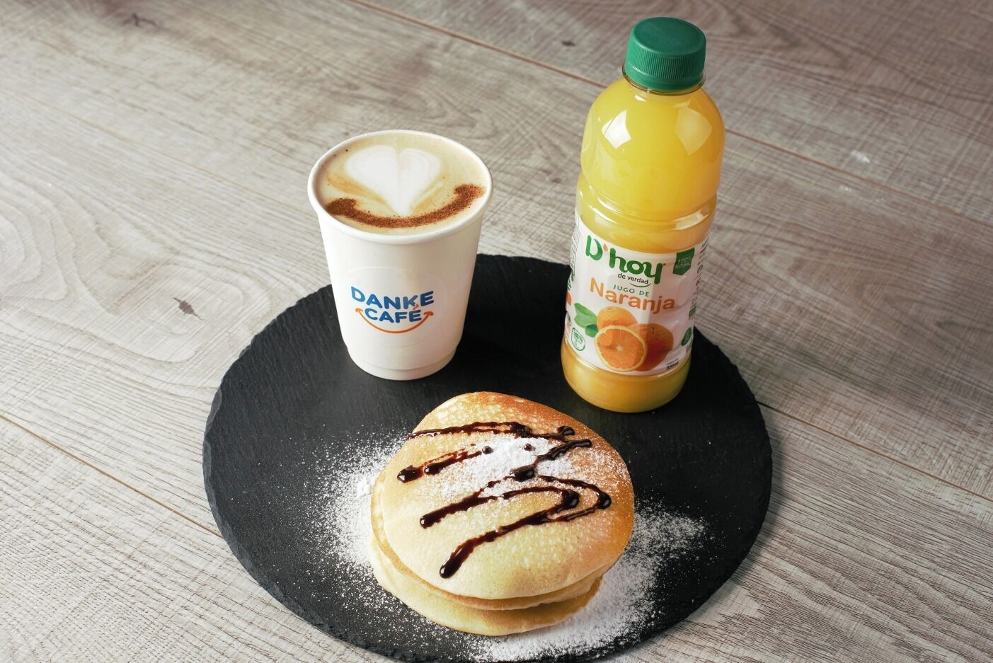 A plate with pancakes, a coffee cup, and a bottle of orange juice on a wooden table.