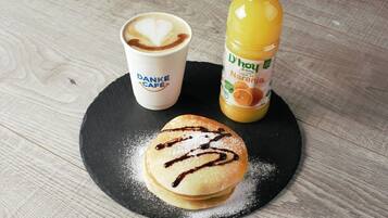 A plate with pancakes, a coffee cup, and a bottle of orange juice on a wooden table.