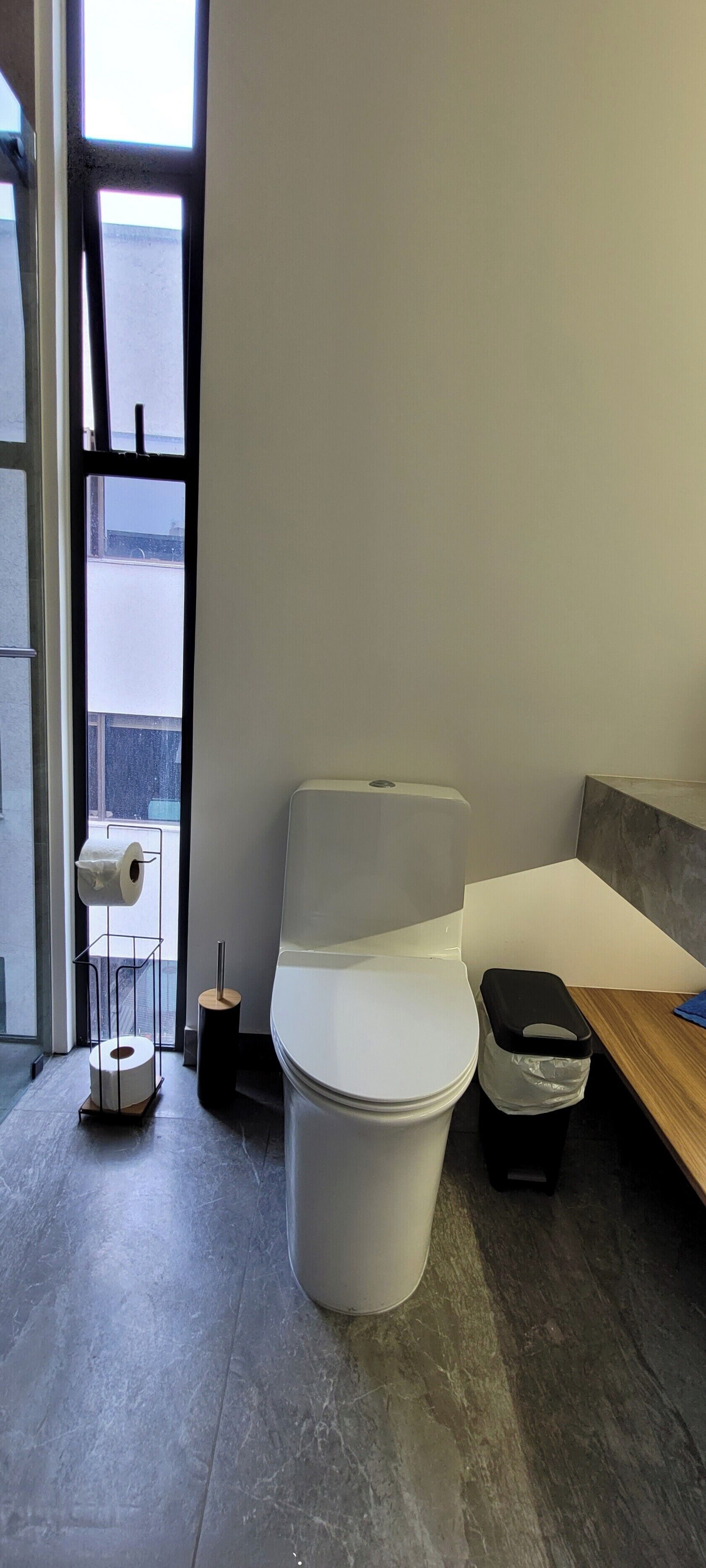 A modern bathroom with a toilet, a paper towel dispenser, and a trash bin.