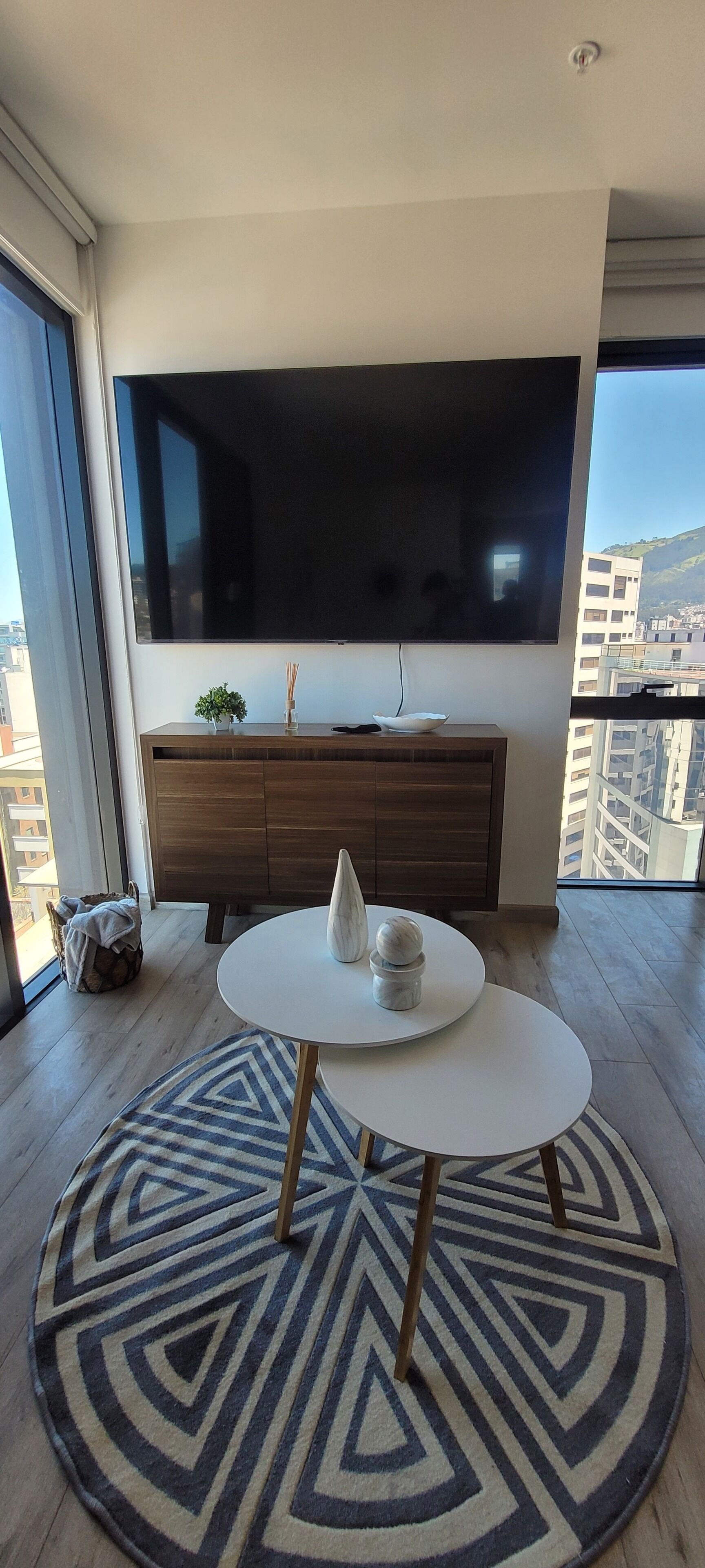 Un salon moderne doté d’un grand téléviseur à écran plat, d’une table ronde agrémentée d’objets décoratifs, d’un tapis à motifs et d’un meuble en bois.