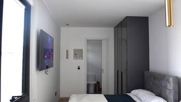 Ein modernes Hotelzimmer mit Bett, Wandfernseher, Kleiderschrank und Fenster.