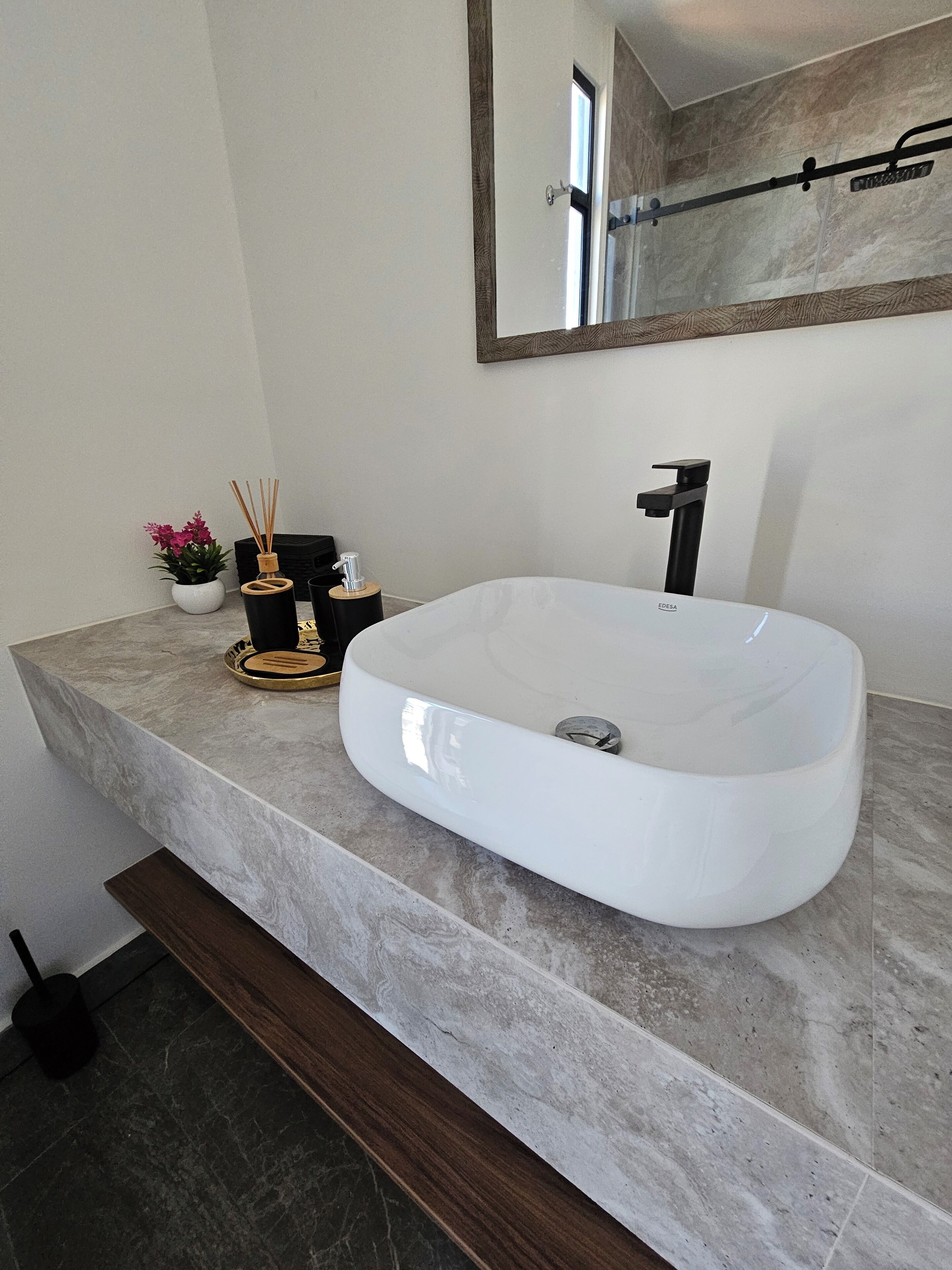 A modern bathroom with a large, white vessel sink, a mirror above it, and a small potted plant on the countertop.