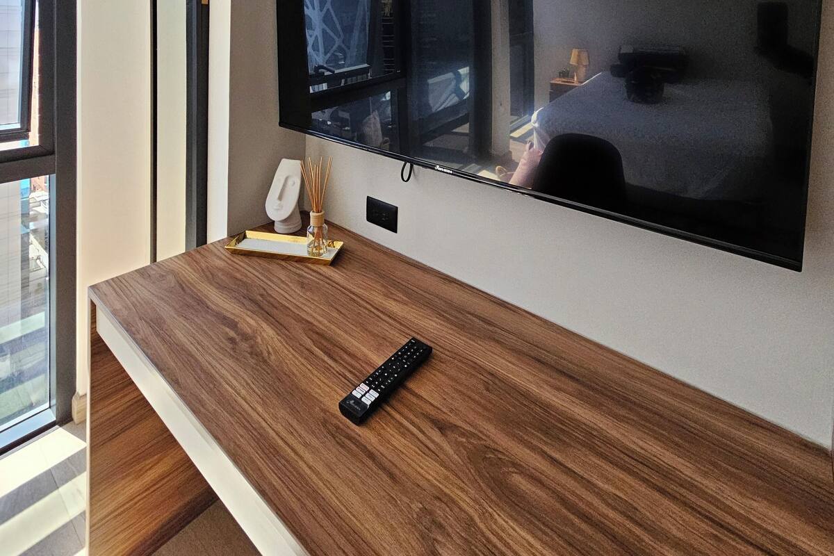 A modern kitchen with a large flat-screen TV mounted on the wall, a wooden countertop, a clock, and a small plant.