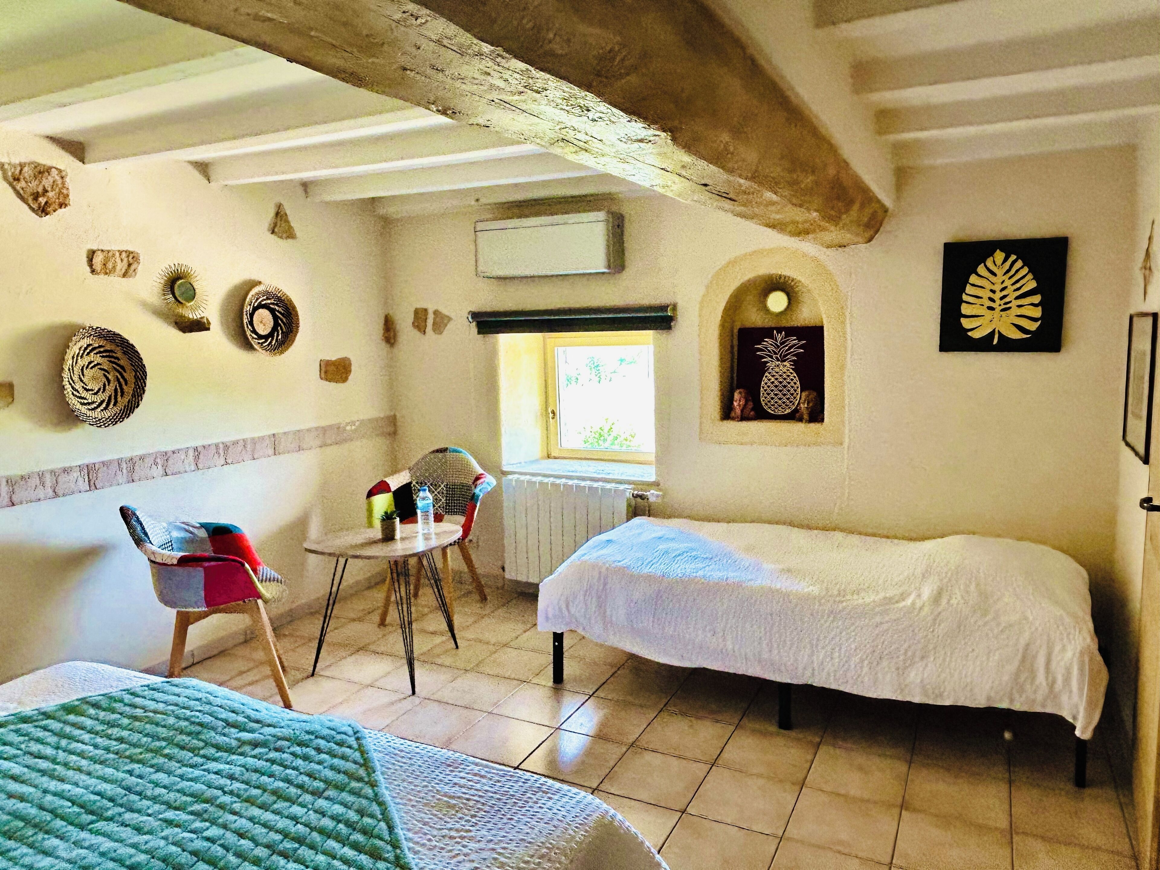 Una habitación con dos camas, una mesita con sillas, un ventanal y decoración en la pared.