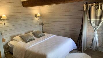 Un dormitorio con cabecera de madera, cama con ropa blanca, dos lámparas de pared y una cortina.