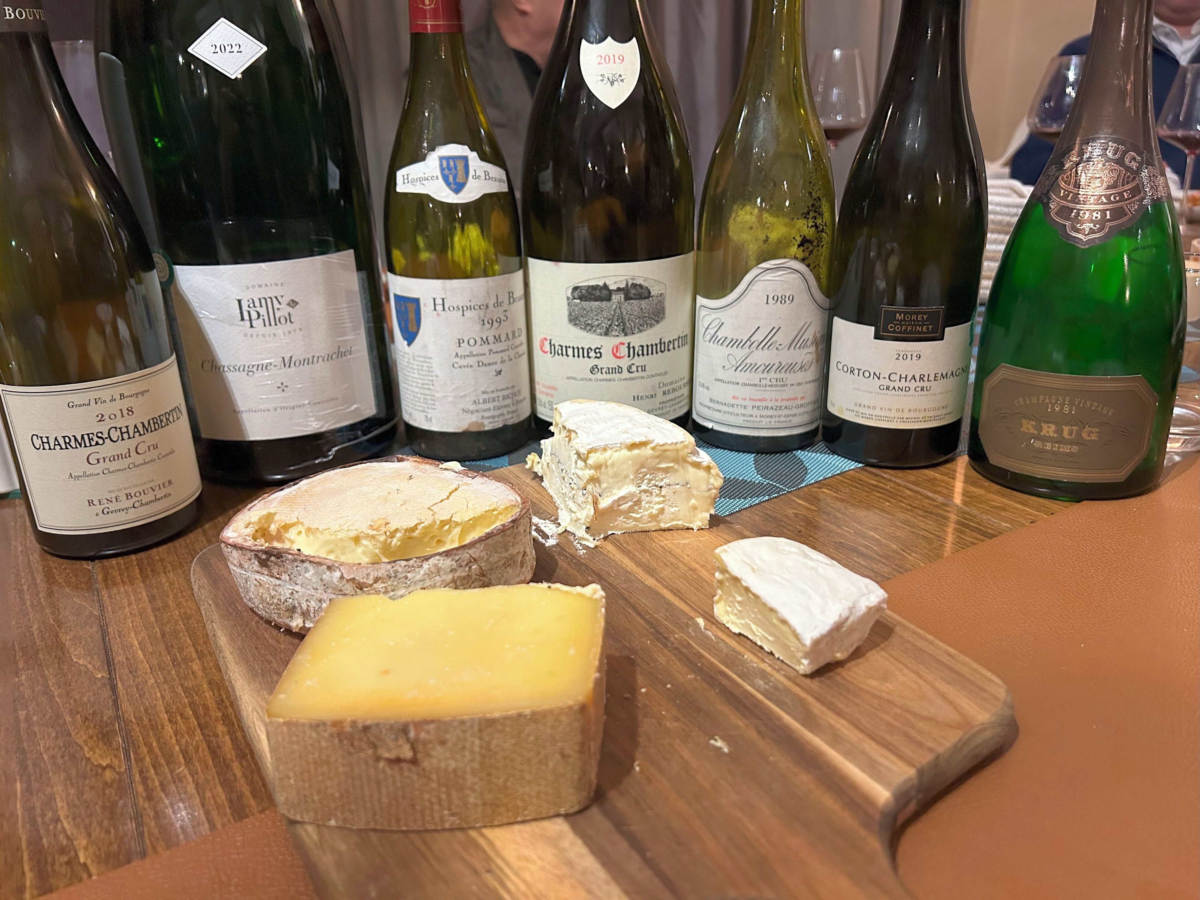 A selection of wine bottles and cheese on a wooden table.