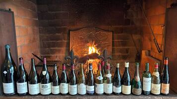A row of wine bottles in front of a brick fireplace with a fire burning.