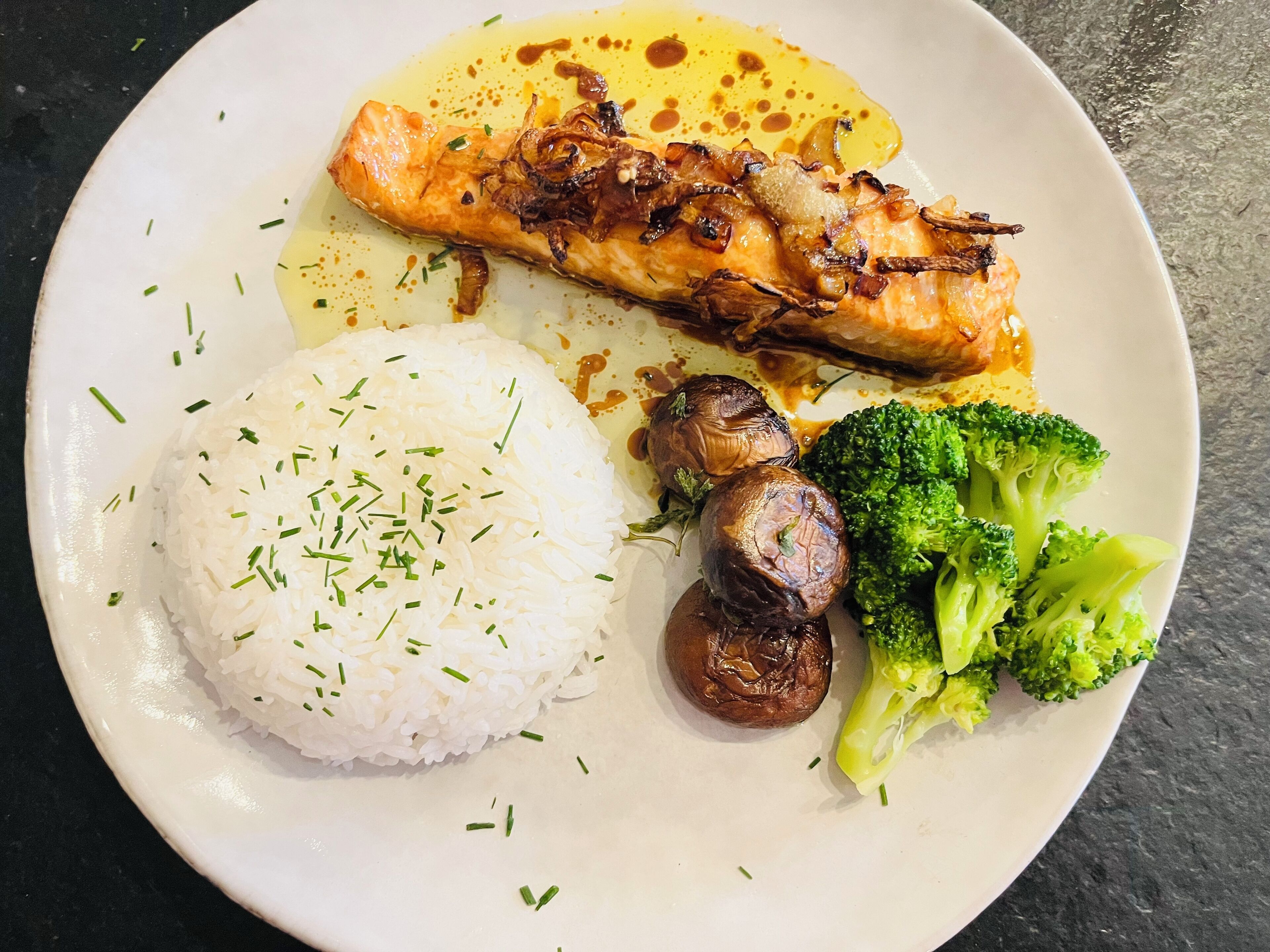 A plate with white rice, broccoli, mushrooms, and a piece of salmon.
