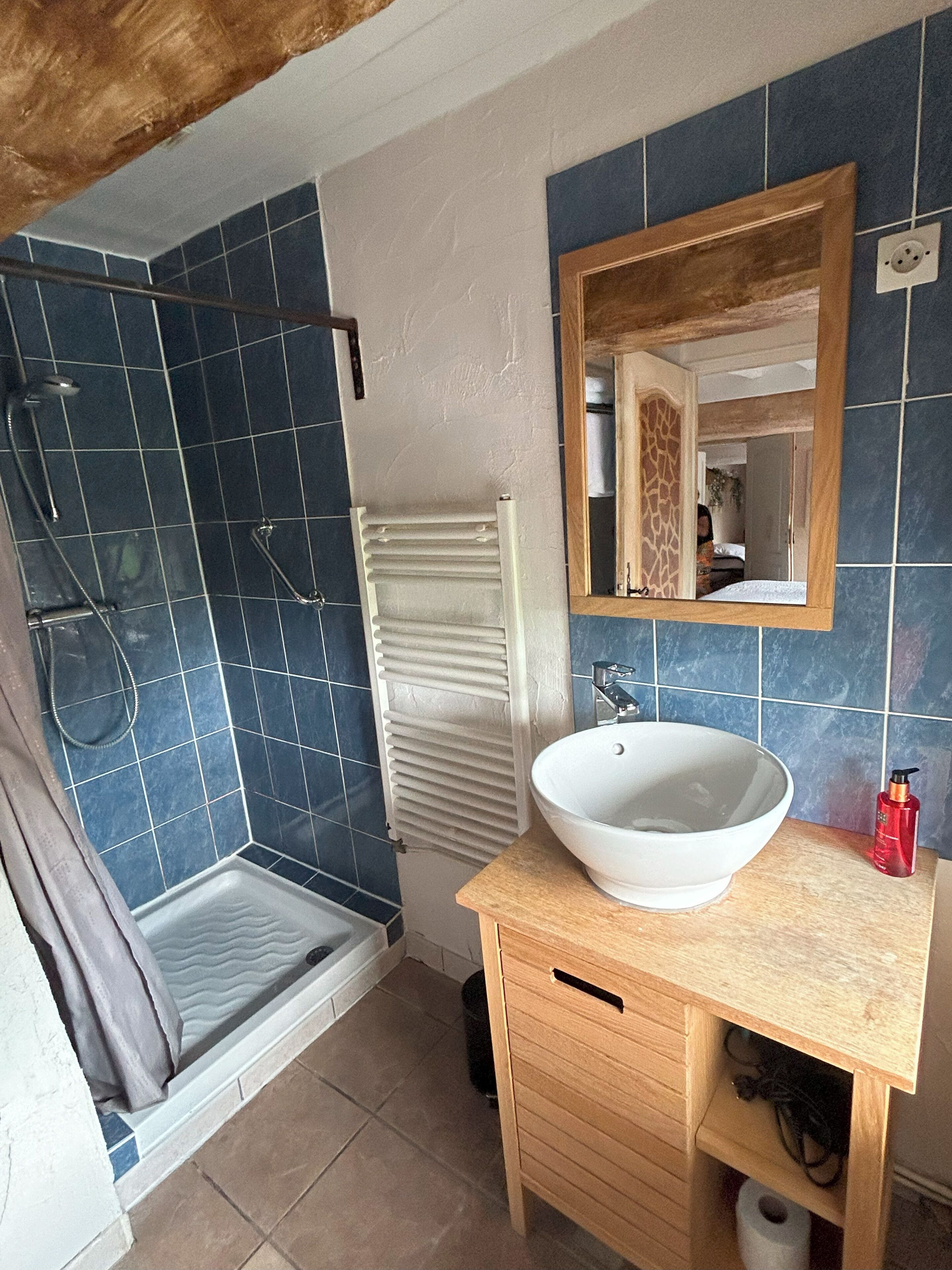 A bathroom with a shower, a sink, a mirror, and a towel rack.