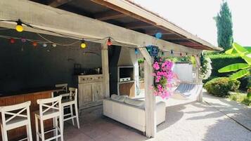 An outdoor patio with a dining area, a sofa, and a hanging flower arrangement.