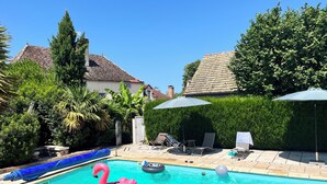 Una piscina con juguetes inflables, un porche cubierto y un jardín bien cuidado.