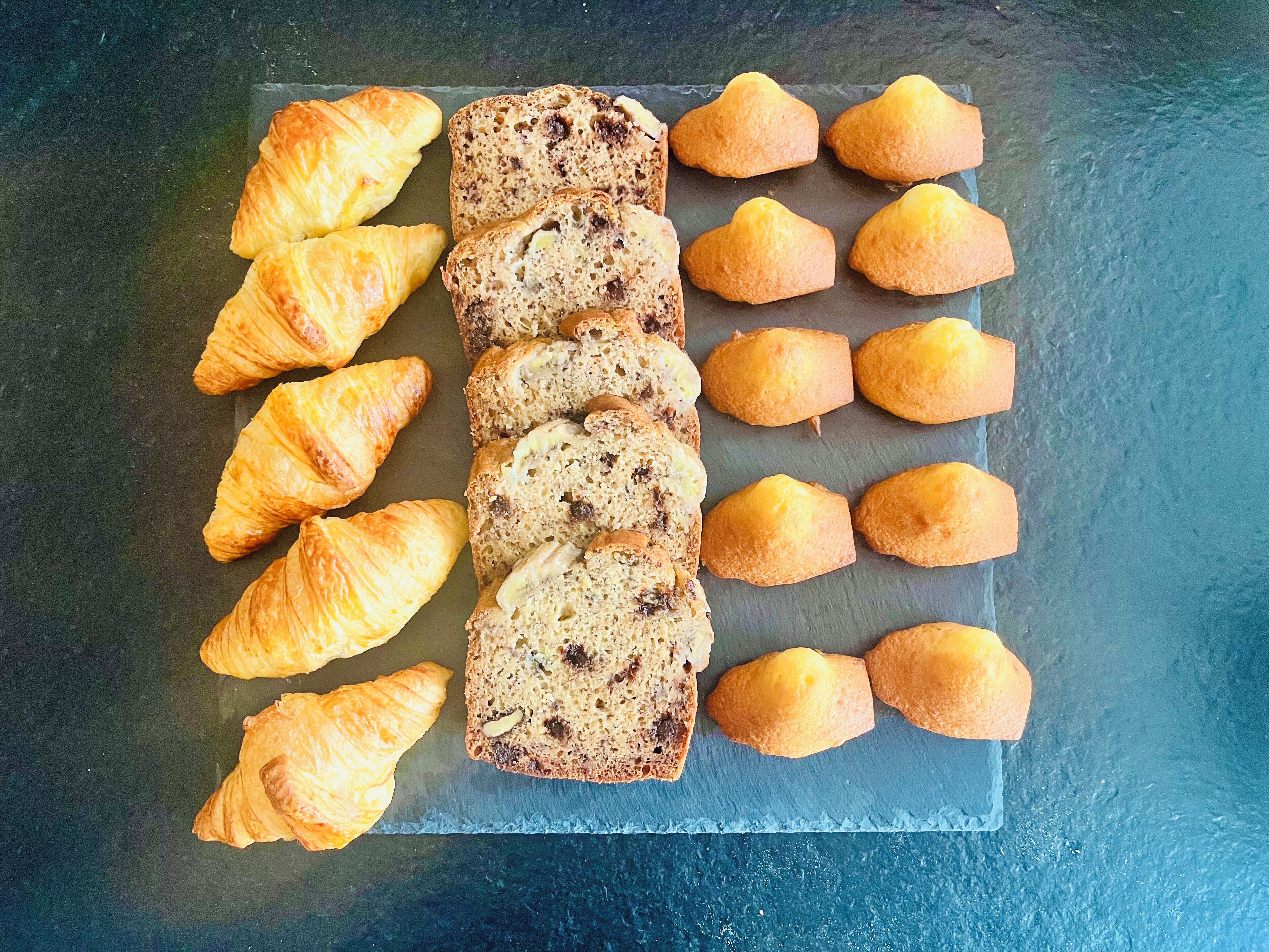Une variété de viennoiseries présentées sur une planche d’ardoise, notamment des croissants et du pain parsemé de graines.