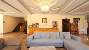A spacious lobby with a large grey sectional sofa, a marble coffee table, a wooden reception desk, a staircase, and a chandelier. - Paro Grand Resort (Paro)